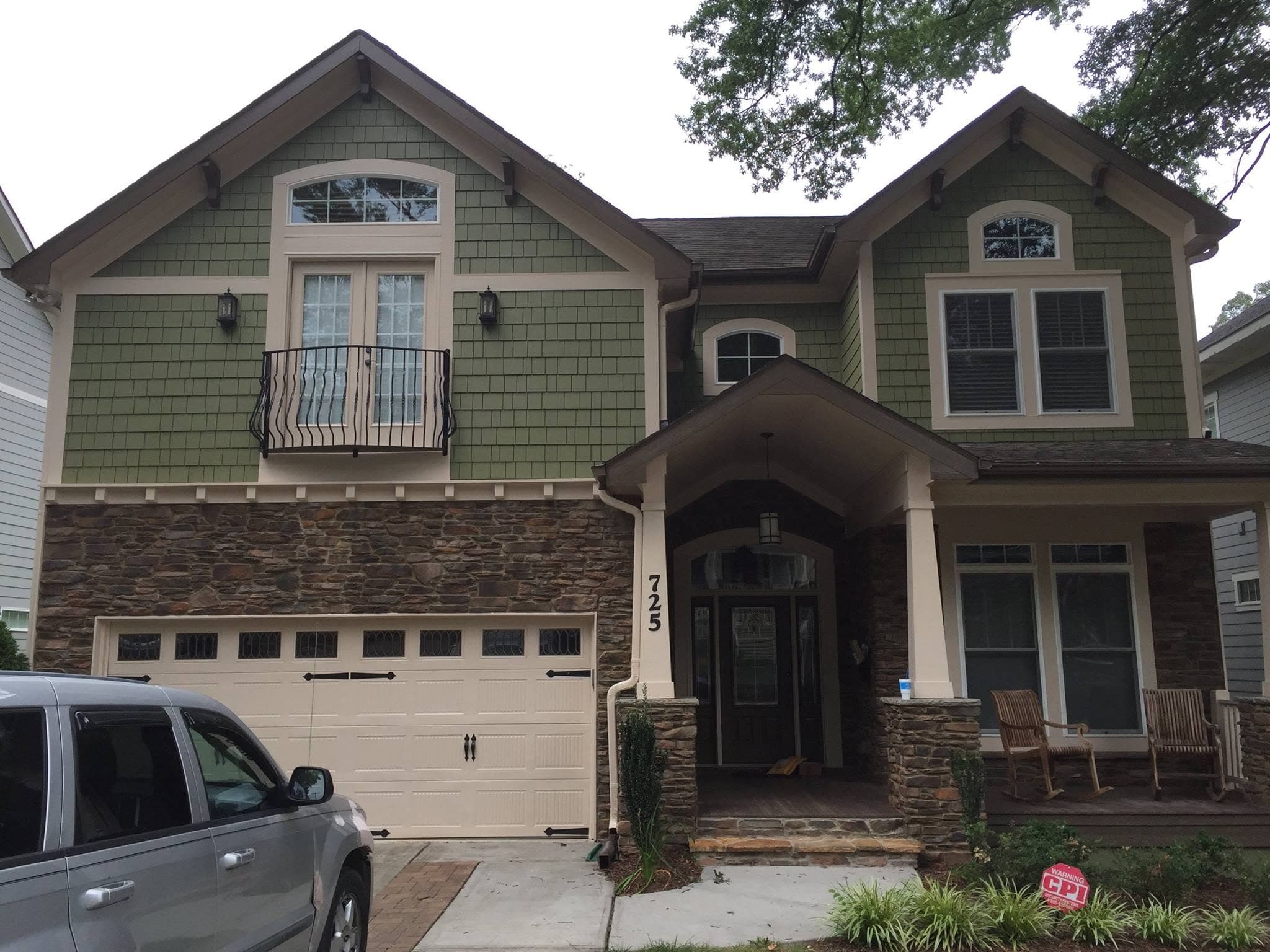 The same house after repainting, with warmer green siding, cream trim, a cream garage door and a repainted porch surround.
