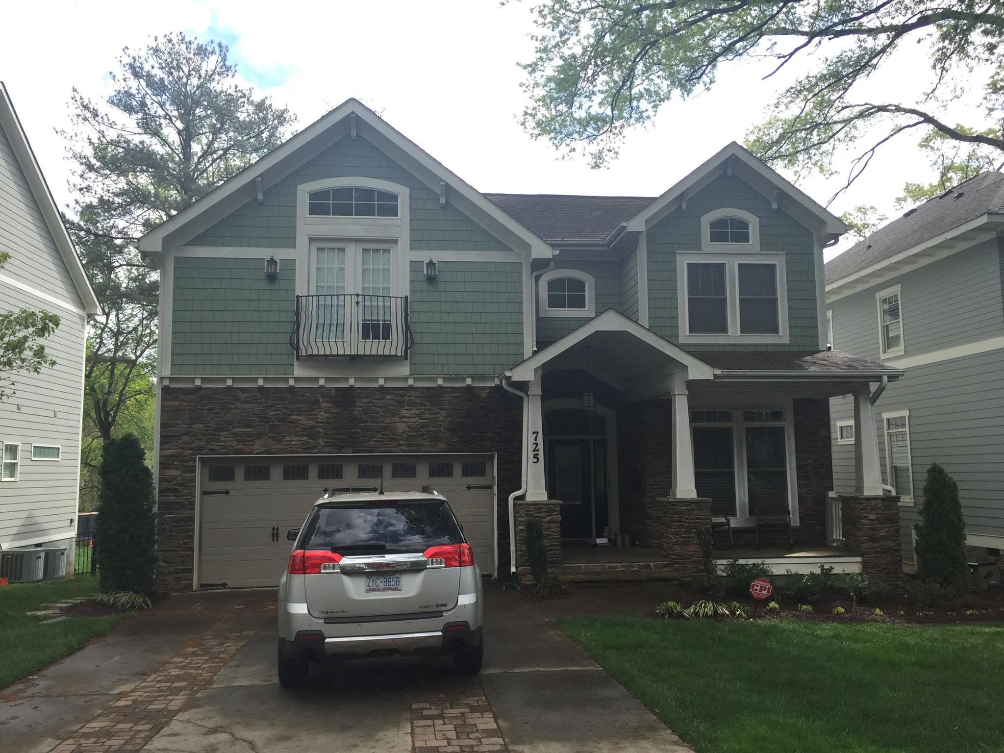 Two-storey craftsman house before repainting, with sage green siding and dark bronze trim and garage door.