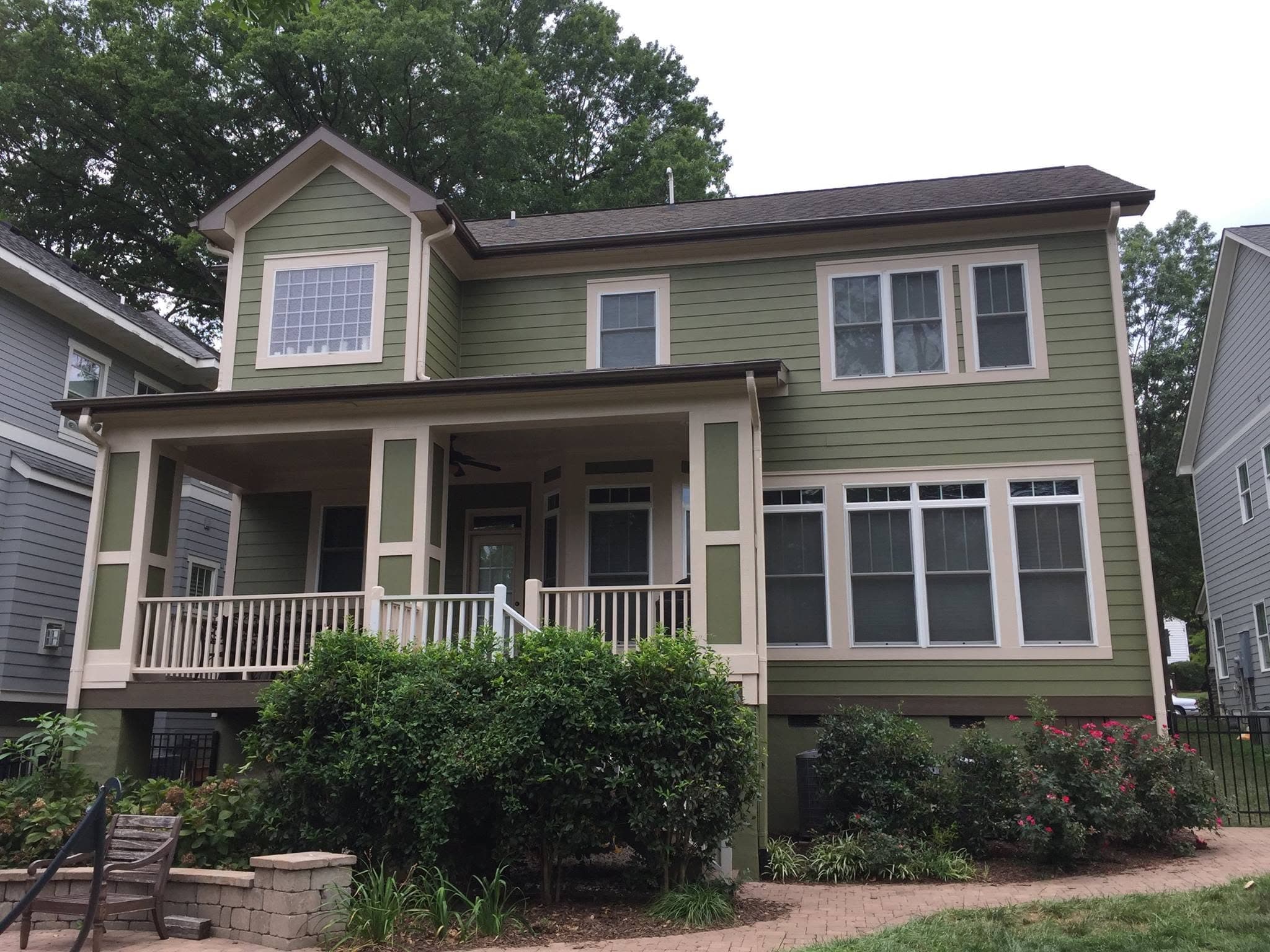 The same house after repainting, with a deeper green body, cream trim and dark porch railings, and the frontage cleared.