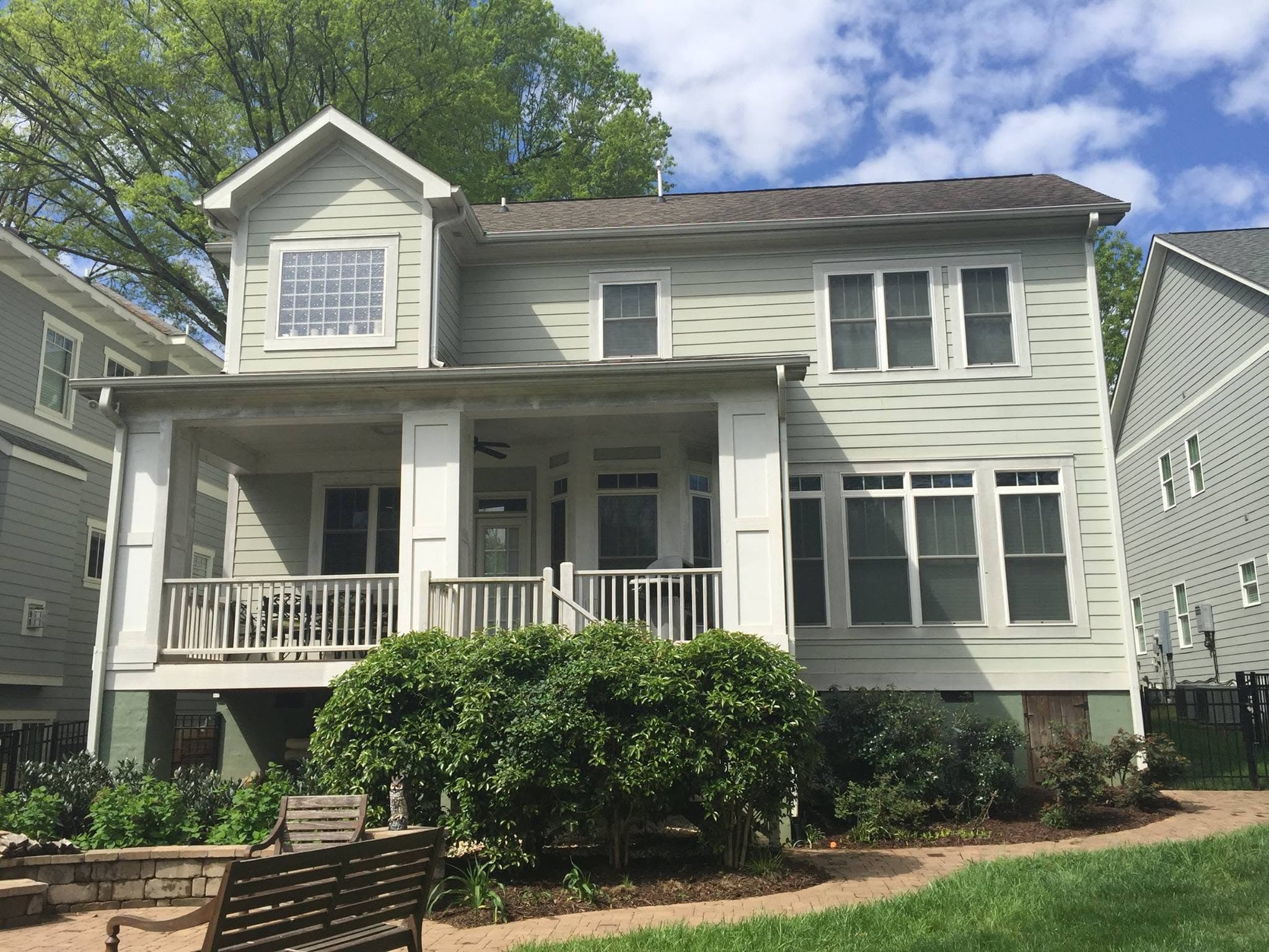 Two-storey house before repainting, with pale sage siding, white trim and overgrown shrubs across the front.