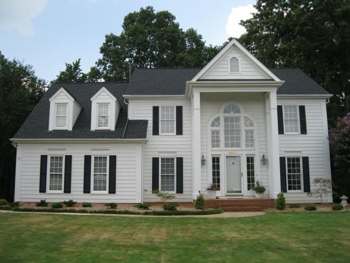White colonial house with black shutters and a painted portico, framed by clipped shrubs.