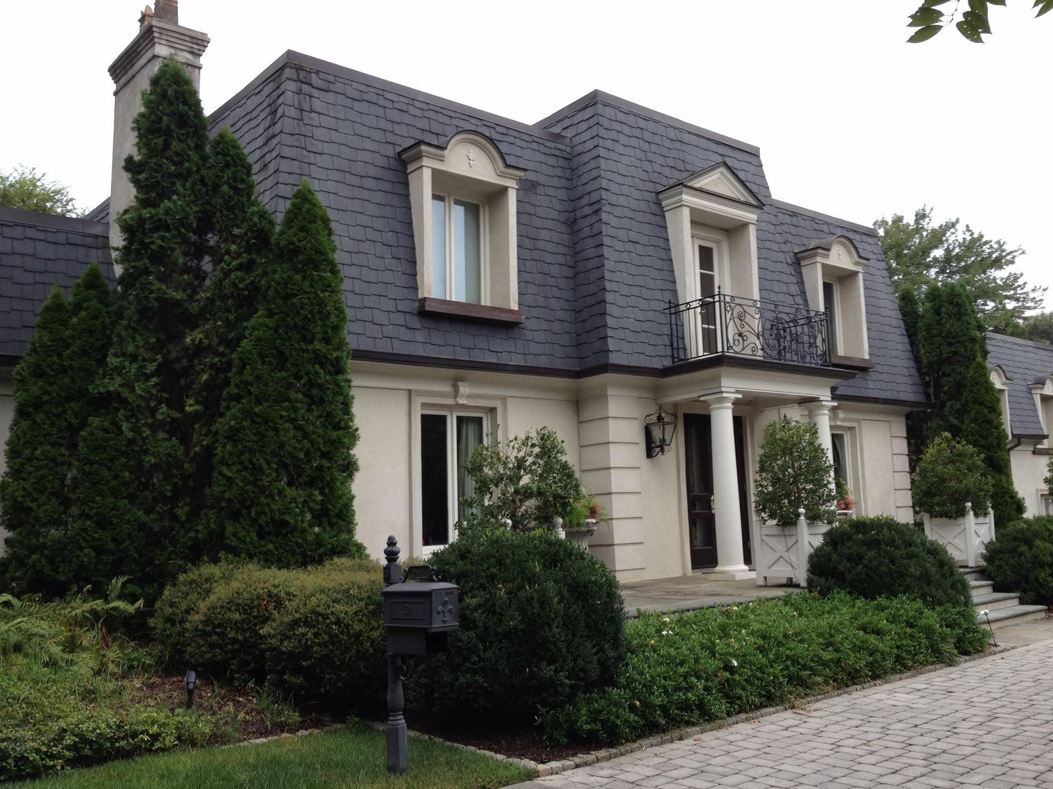 Cream-painted house with tall shuttered windows, a slate roof and mature hedging along the frontage.