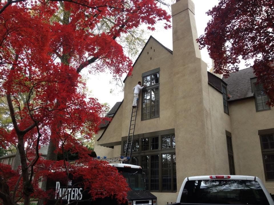 Ladder set against a stucco and timber house mid-job, with a red Japanese maple in the foreground.