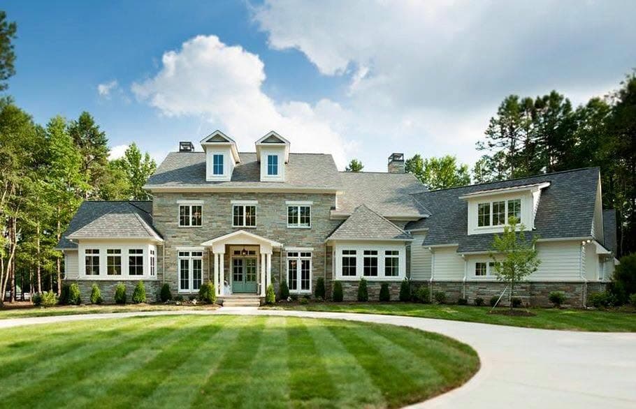 Large shingle-style home with a painted exterior and white trim, photographed across a wide front lawn on a clear day.
