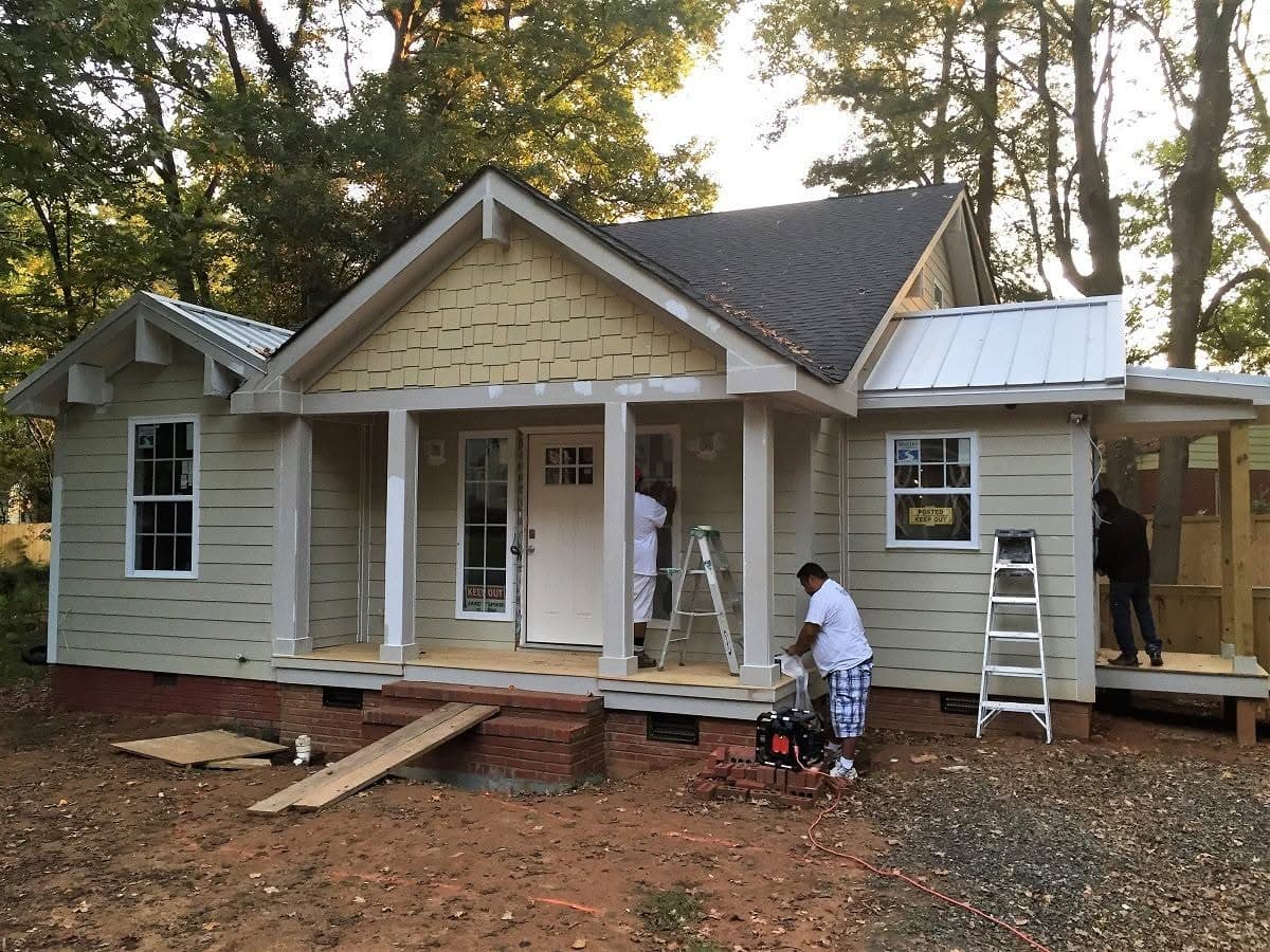 Single-storey craftsman bungalow mid-job, siding unpainted, ladders and crew working on the front porch.