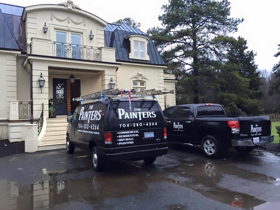 The Painters branded van and truck parked on the drive of a large cream-painted house on a wet day.