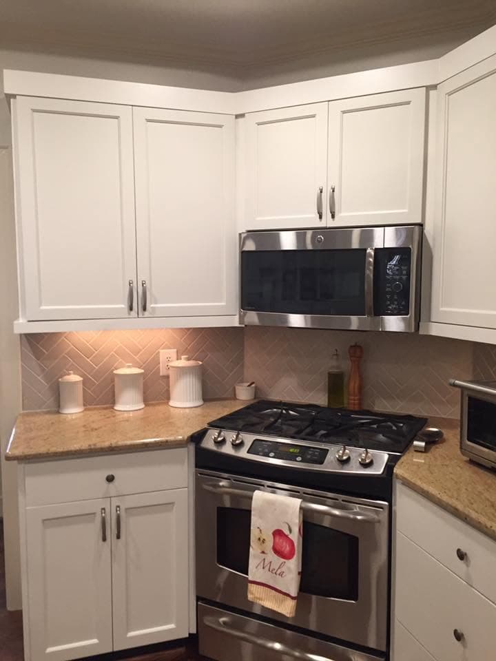 Finished kitchen corner with off-white cabinets above a tiled splashback and gas range.