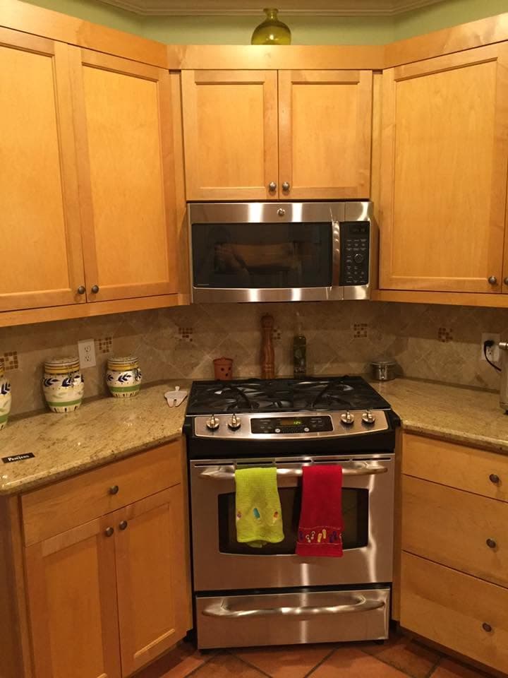 Kitchen corner before painting, with honey oak wall and base cabinets around a gas range and microwave.